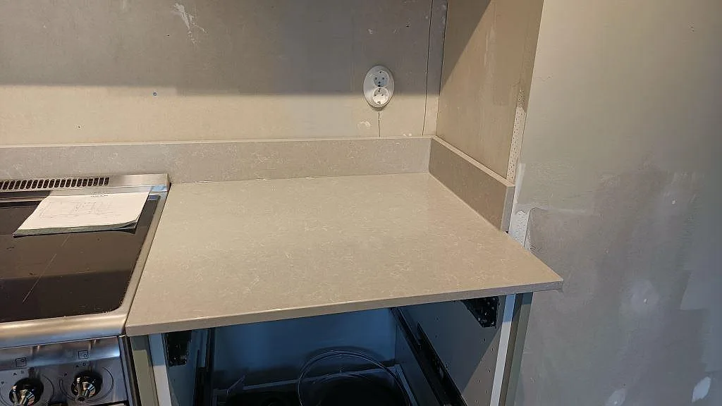 Bänkskiva i Technistone Noble Ivory White intill den fristående induktionsspisen med låg uppvikt stänkkant i ett kök i Klagshamn.