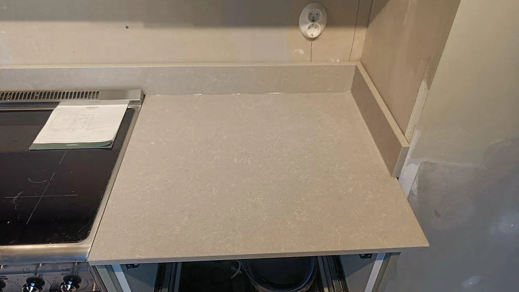 Detalj av den ivoryfärgade Technistone Noble Ivory White-bänkskivan med diskret melerad yta intill spisen i ett kök i Klagshamn.