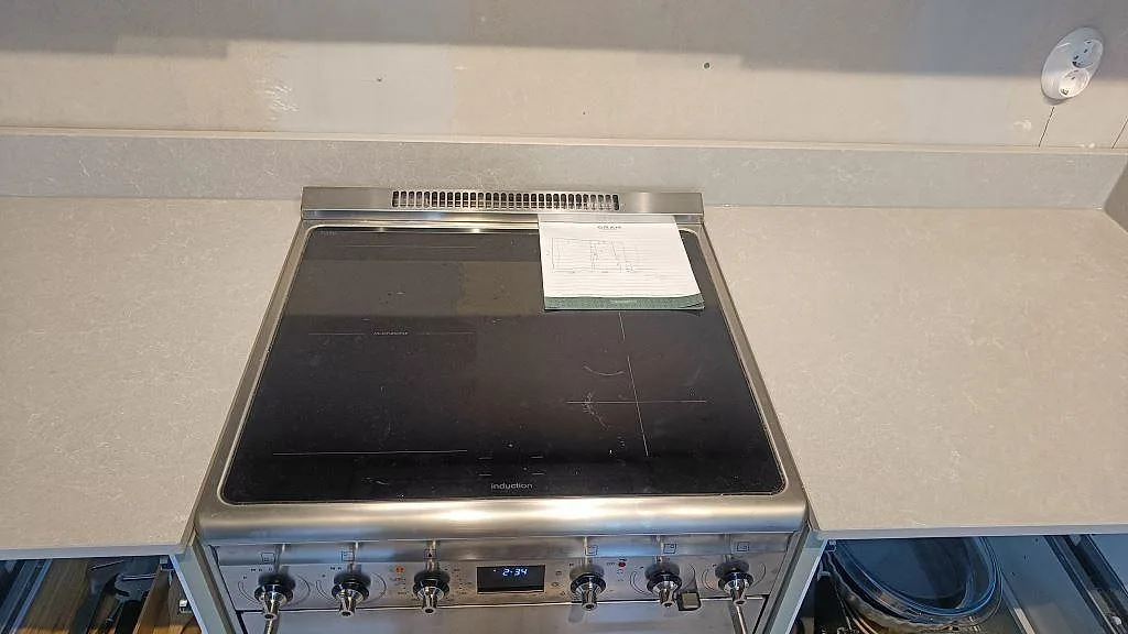 Fristående induktionshäll inbäddad mellan bänkskivor i Technistone Noble Ivory White i ett kök i Klagshamn.