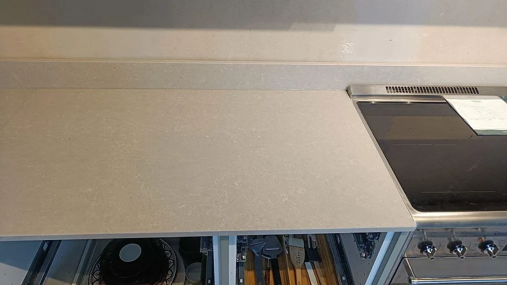Lång bänkskiveyta i Technistone Noble Ivory White ovanför öppna lådor i ett kök under inredning i Klagshamn.