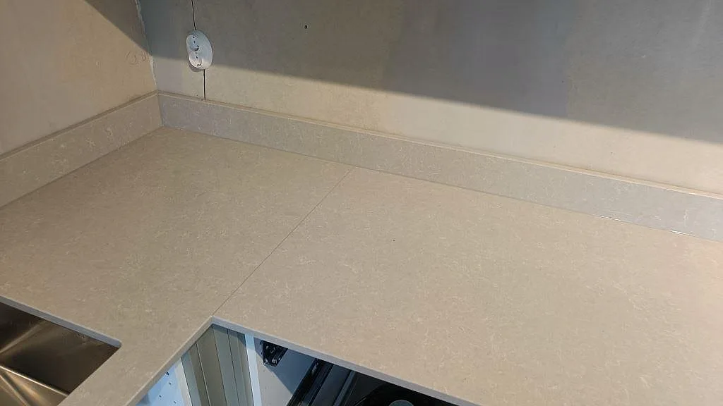 Hörnsektion av köksbänkskivan i Technistone Noble Ivory White med skarv och uppvikt stänkkant samt rostfri hochörna i Klagshamn.
