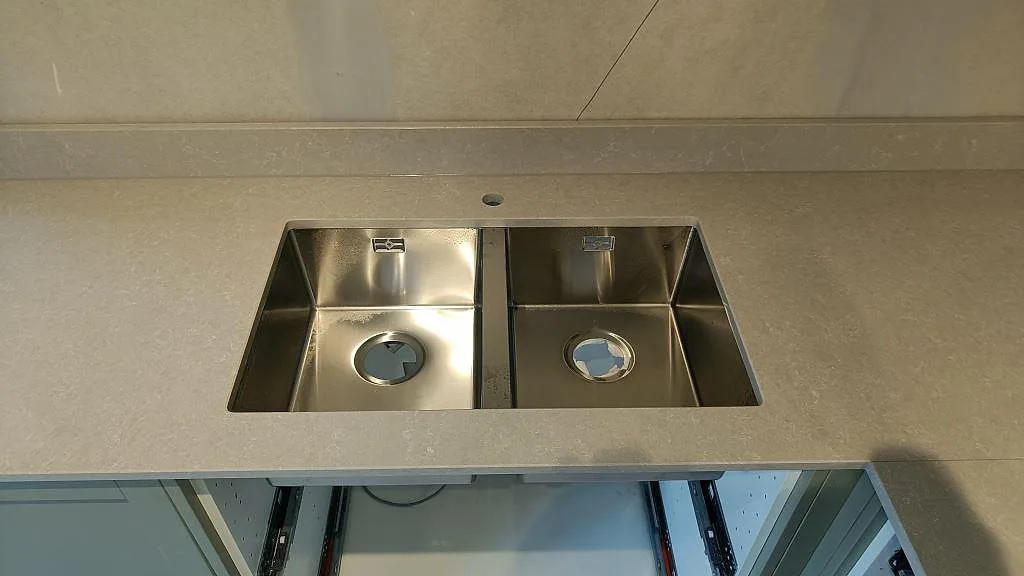 Dubbelhoad underlimmad rostfri diskho infälld under bänkskivan i Technistone Noble Ivory White i ett kök i Klagshamn.