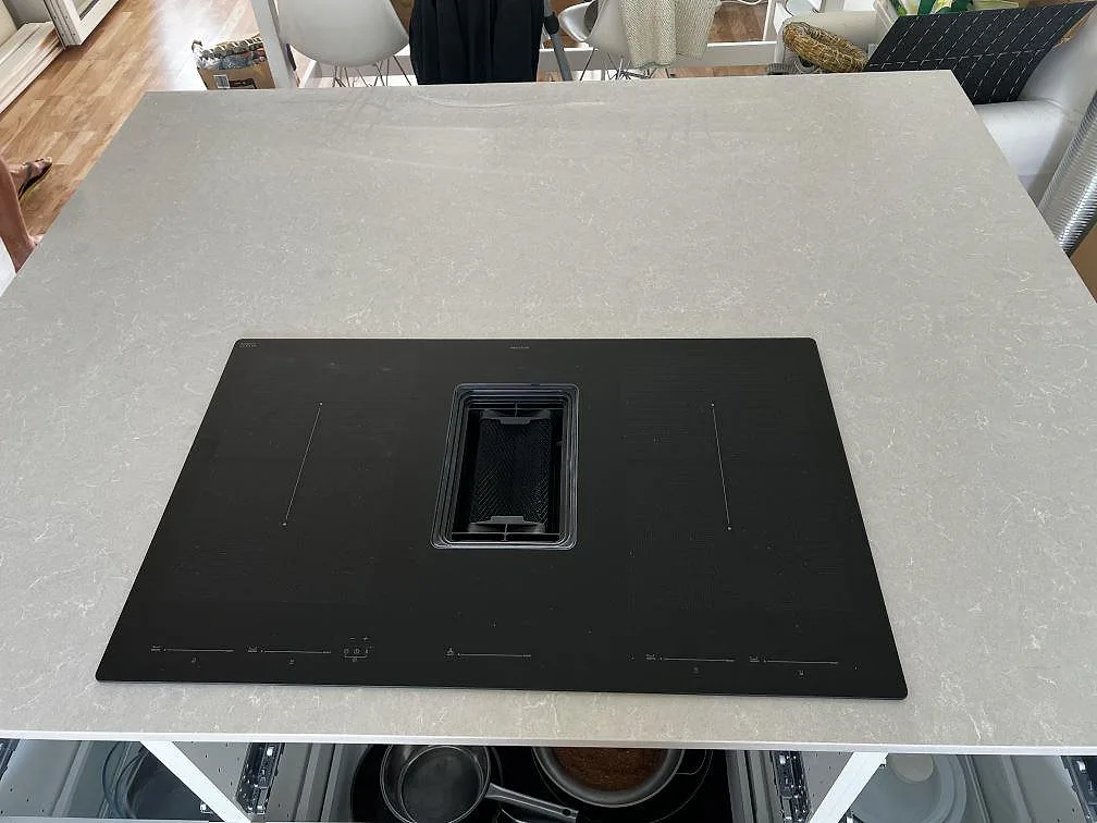 Köksö med polerad Technistone Noble Ivory White och svart induktionshäll i ett vitt kök under montering i Klagshamn.