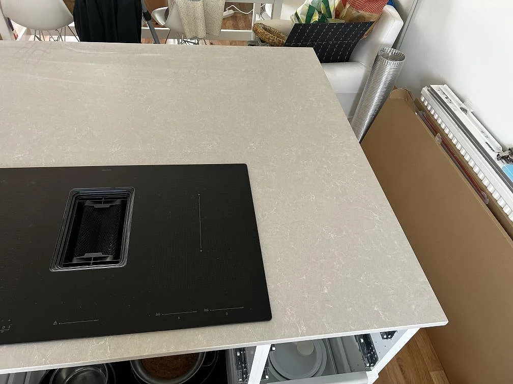 Närbild av polerad Technistone Noble Ivory White runt svart induktionshäll på köksö i Klagshamn.