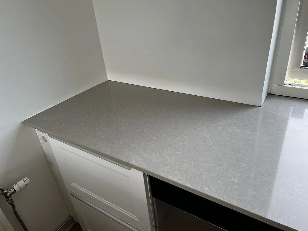 Sidobänk i polerad Technistone Noble Ivory White, ljus kvartskomposit, monterad mot vita stommar i köket i Klagshamn.