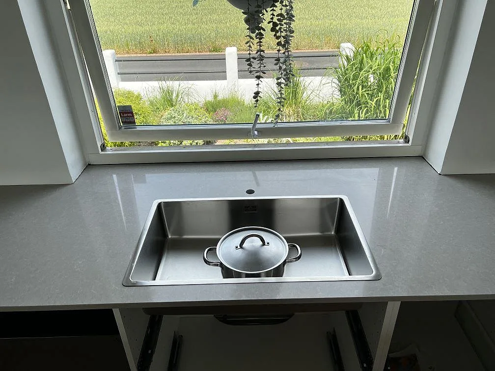 Köksbänkskiva i polerad Technistone Noble Ivory White, ljus kvartskomposit, med underlimmad rostfri diskho under fönster i Klagshamn.