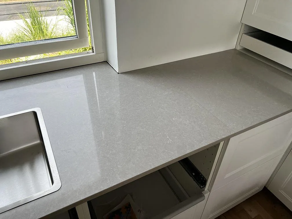Köksbänkskiva i Technistone Noble Ivory White vid fönster med rostfri diskho och vita köksstommar i Klagshamn.