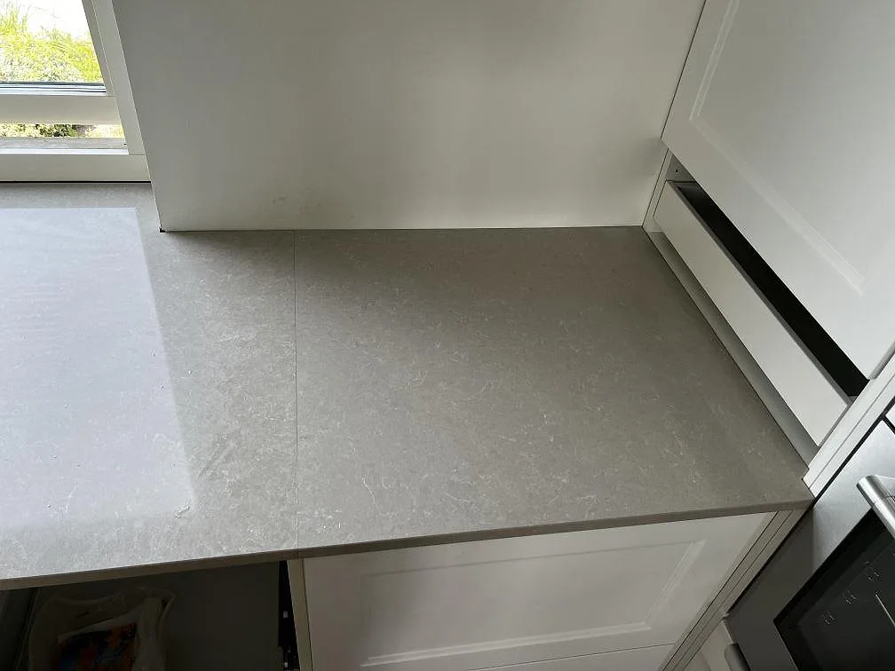 Hörnpassad köksbänk i polerad Technistone Noble Ivory White med ljus yta och vita luckor i Klagshamn.