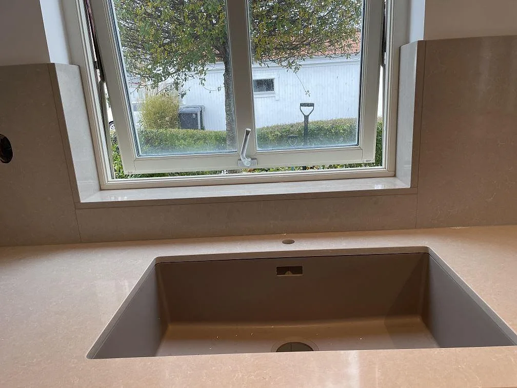 Underlimmad diskho i bänkskiva av polerad Technistone Noble Ivory White komposit vid fönster i Klagshamn.