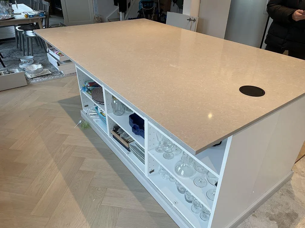 Detalj av stor köksö i Technistone Noble Ivory White, polerad komposit, med kabelgenomföring i Klagshamn.
