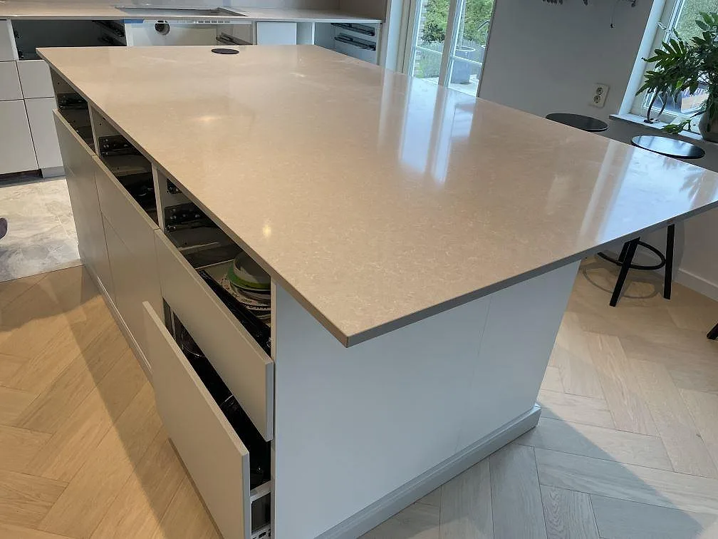 Polerad köksö i Technistone Noble Ivory White med ljus ådring och öppna lådor under montering i Klagshamn.