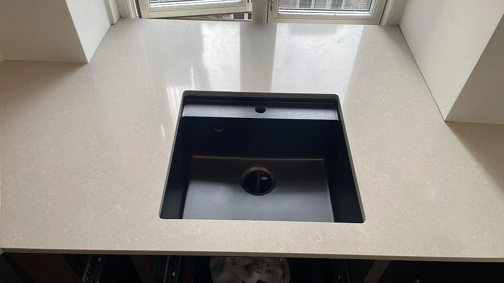 Närbild på svart diskho i polerad Technistone Noble Ivory White komposit med ljus marmorerad yta i kök i Köpenhamn.
