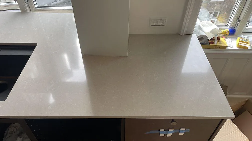 Bred bänkyta i polerad Technistone Noble Ivory White komposit bredvid svart diskho och fönsternisch i Köpenhamn.