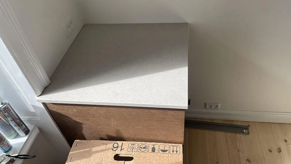 Mindre bänkskiva i polerad Technistone Noble Ivory White komposit vid vägg och fönster under montering i Köpenhamn.