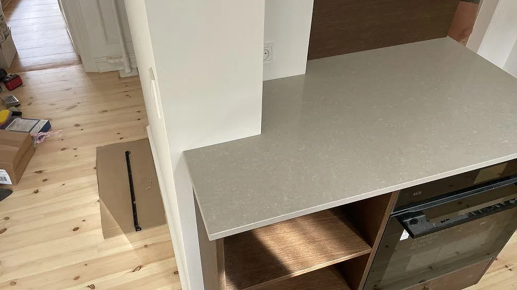 Sidoyta i polerad Technistone Noble Ivory White komposit över trästommar och ugn i ett kök i Köpenhamn.
