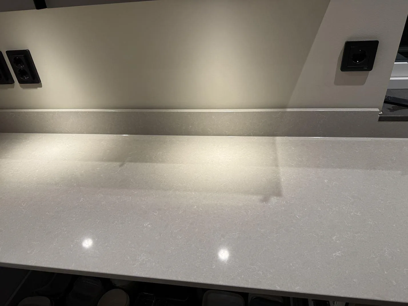 Detalj av polerad Technistone Noble Ivory White som köksbänkskiva med uppvikt stänkkant och ljusa reflexer i Kungsbacka.