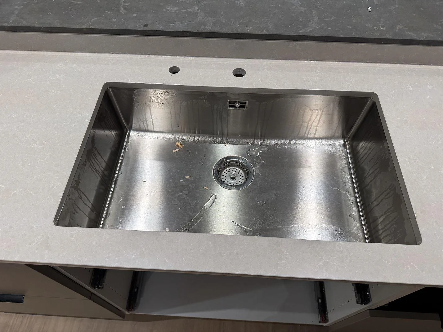 Närbild av rostfri diskho i köksbänkskiva av polerad Technistone Noble Ivory White med blandarhål i Kungsbacka.