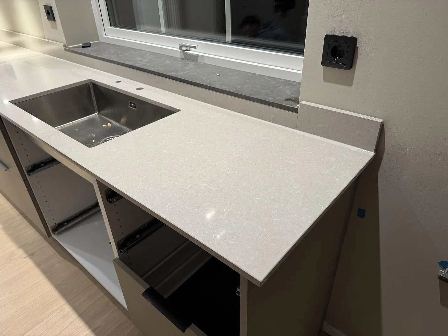 Polerad köksbänkskiva i Technistone Noble Ivory White med rostfri diskho, uppvikt stänkkant och öppen köksstomme under montering i Kungsbacka.