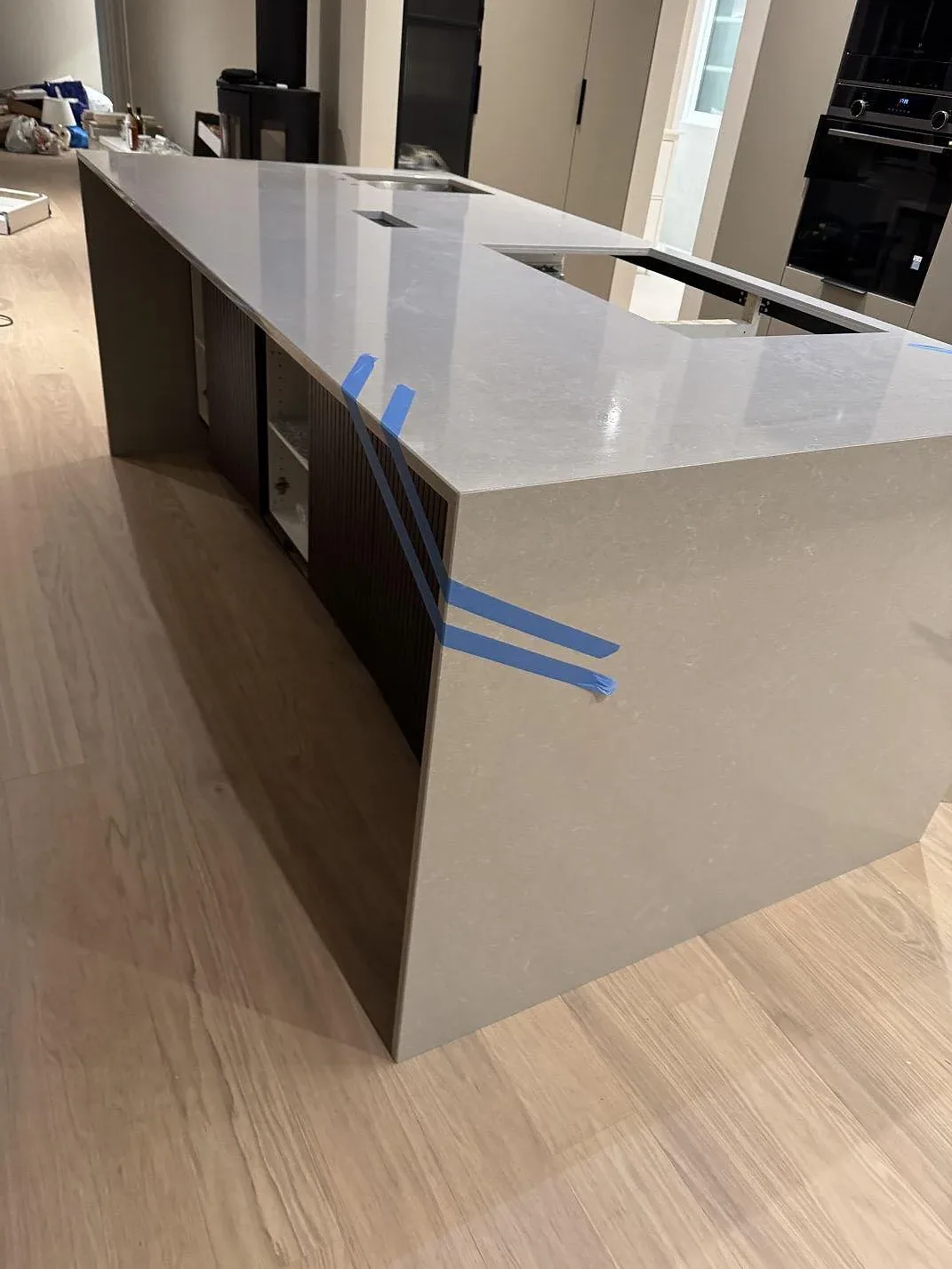 Fristående köksdel i polerad Technistone Noble Ivory White, ljus kvartskomposit, med större rektangulära urtag under montering i Kungsbacka.