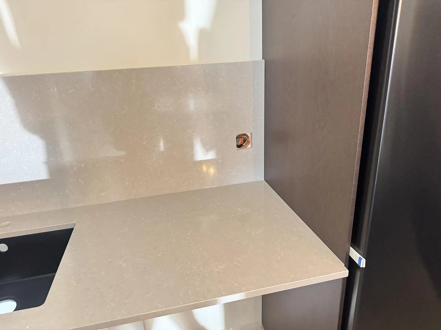 Diskbänkssida i polerad Technistone Noble Ivory White med svart diskho, eluttag i stänkskyddet och mörkt högskåp i Kungsbacka.
