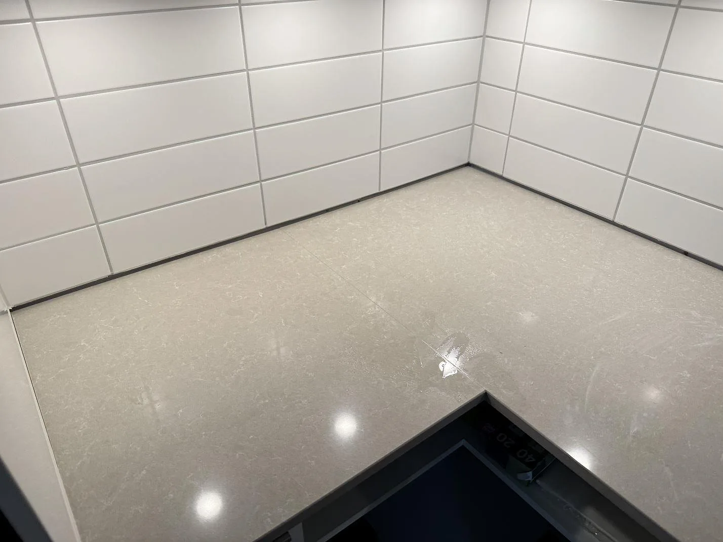 L-format hörn av köksbänkskiva i polerad Technistone Noble Ivory White med ljus ådring och kaklad vägg i Landskrona.