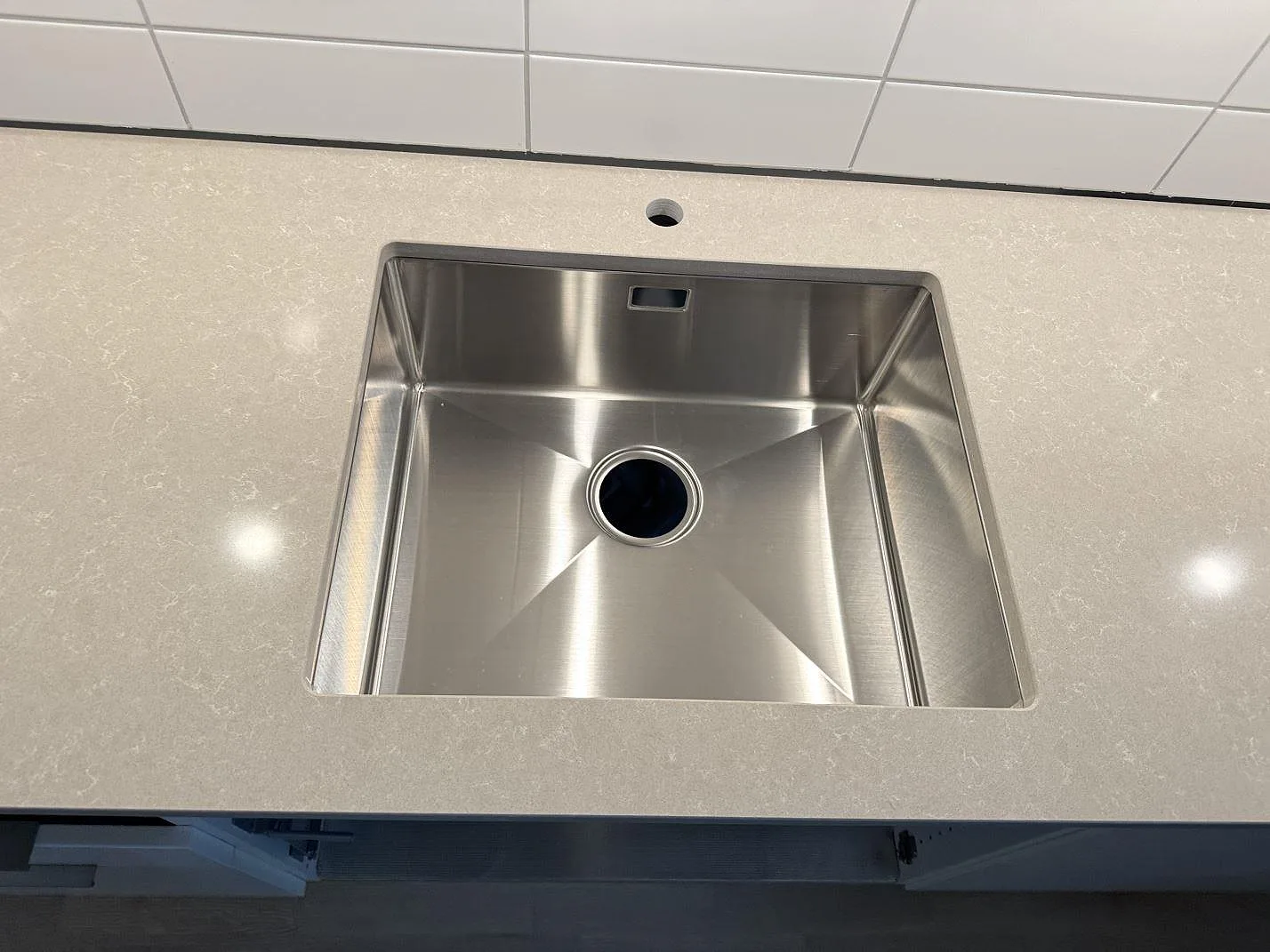 Närbild av underlimmad rostfri diskho i en polerad Technistone Noble Ivory White köksbänkskiva med blandarhål i Landskrona.