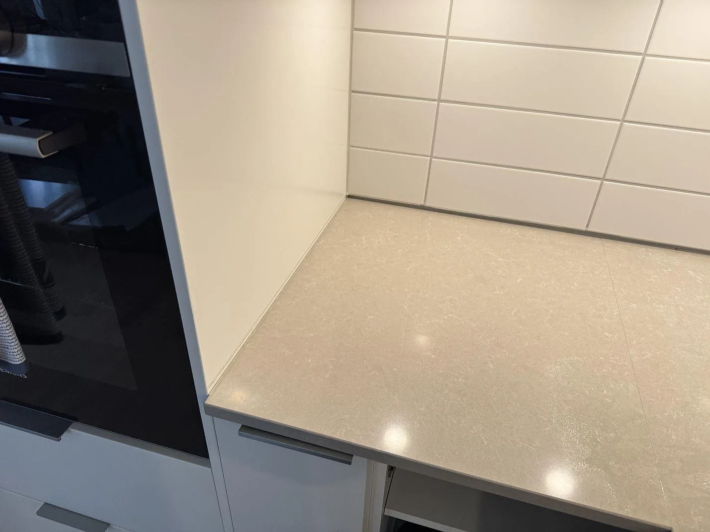 Rak del av köksbänkskiva i polerad Technistone Noble Ivory White bredvid inbyggnadsugn och kaklad vägg i Landskrona.