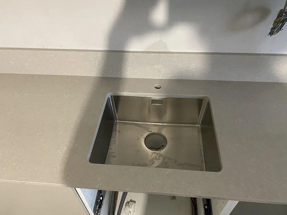 Närbild på underlimmad rostfri diskho i polerad Technistone Noble Ivory White med låg stänkkant i kök i Limhamn.