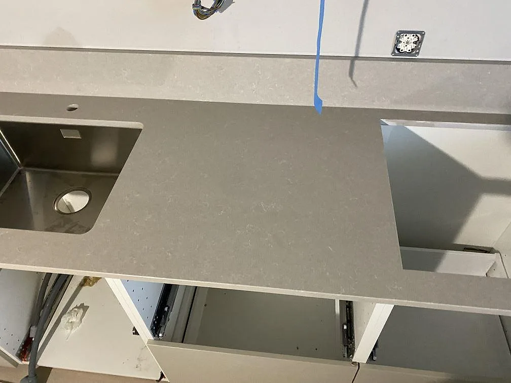 Polerad kvartskompositbänkskiva Technistone Noble Ivory White med rostfri diskho och utskärning för häll under montering i Limhamn.