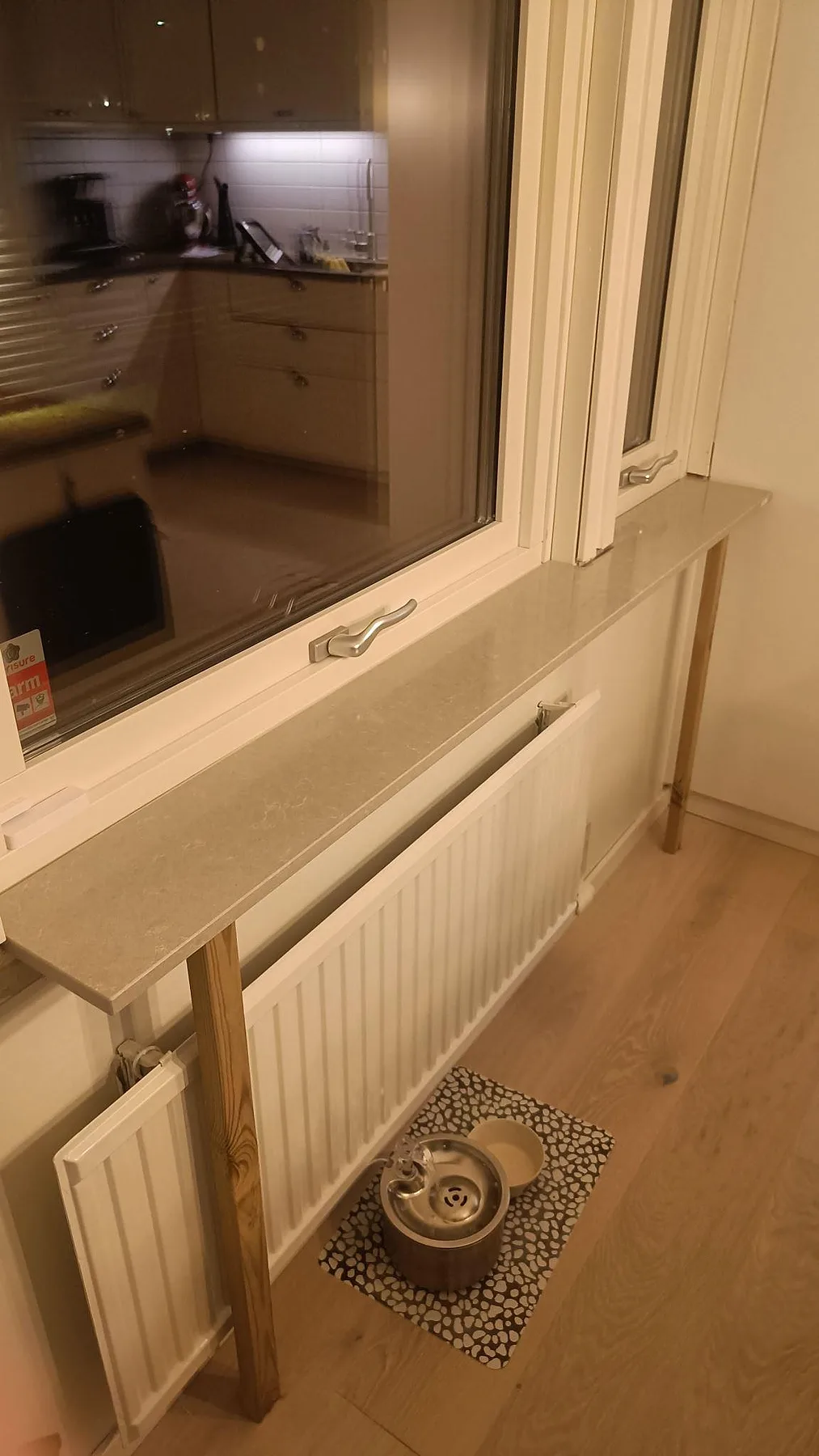 Närbild på lång polerad fönsterbänk i Technistone Noble Ivory White med radiator och tillfälliga trästöd i Löddeköpinge.