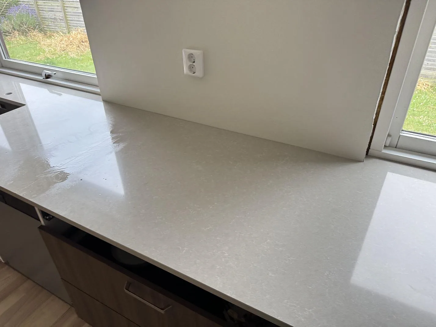 Ljus köksbänkskiva i Technistone Noble Ivory White, polerad komposit, längs fönsterväggen i Löddeköpinge.
