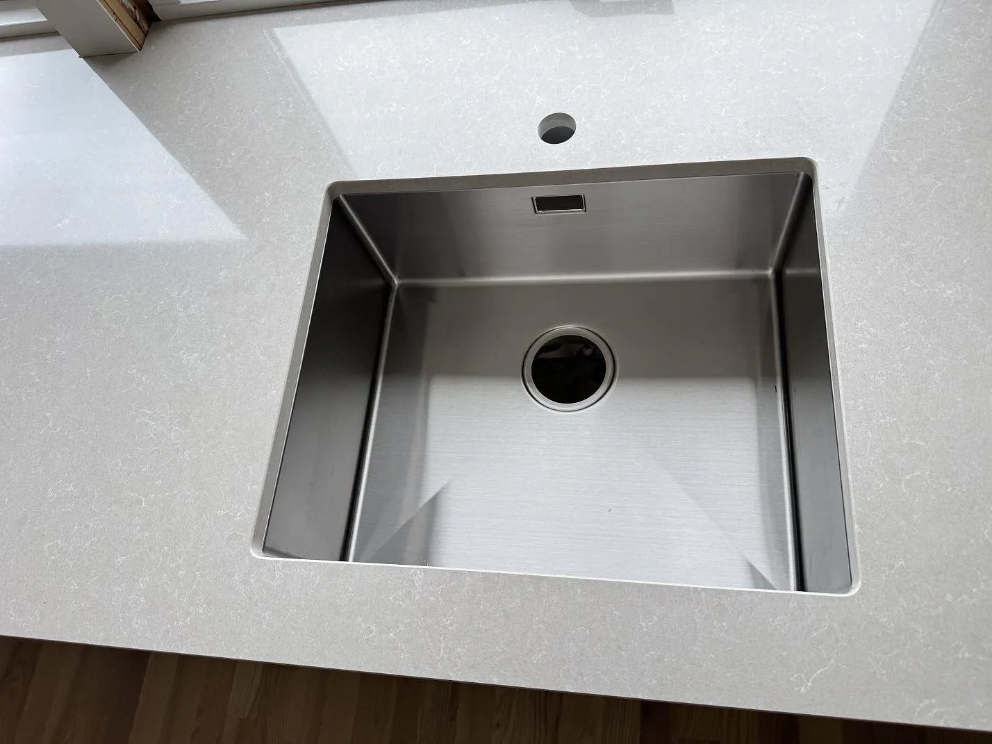 Närbild på rostfri diskho i polerad Technistone Noble Ivory White bänkskiva med blandarhål i Löddeköpinge.