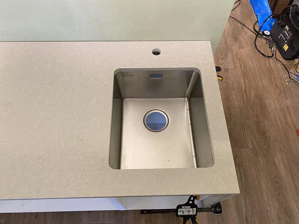 Top-down-bild av rostfri diskho under en polerad köksbänkskiva i Technistone Noble Ivory White i Lomma.