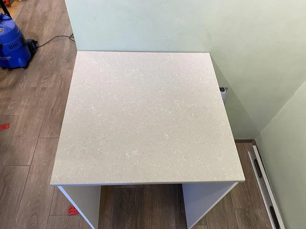 Detalj av kort sidobänk i polerad Technistone Noble Ivory White med ljus ådring i köket i Lomma.