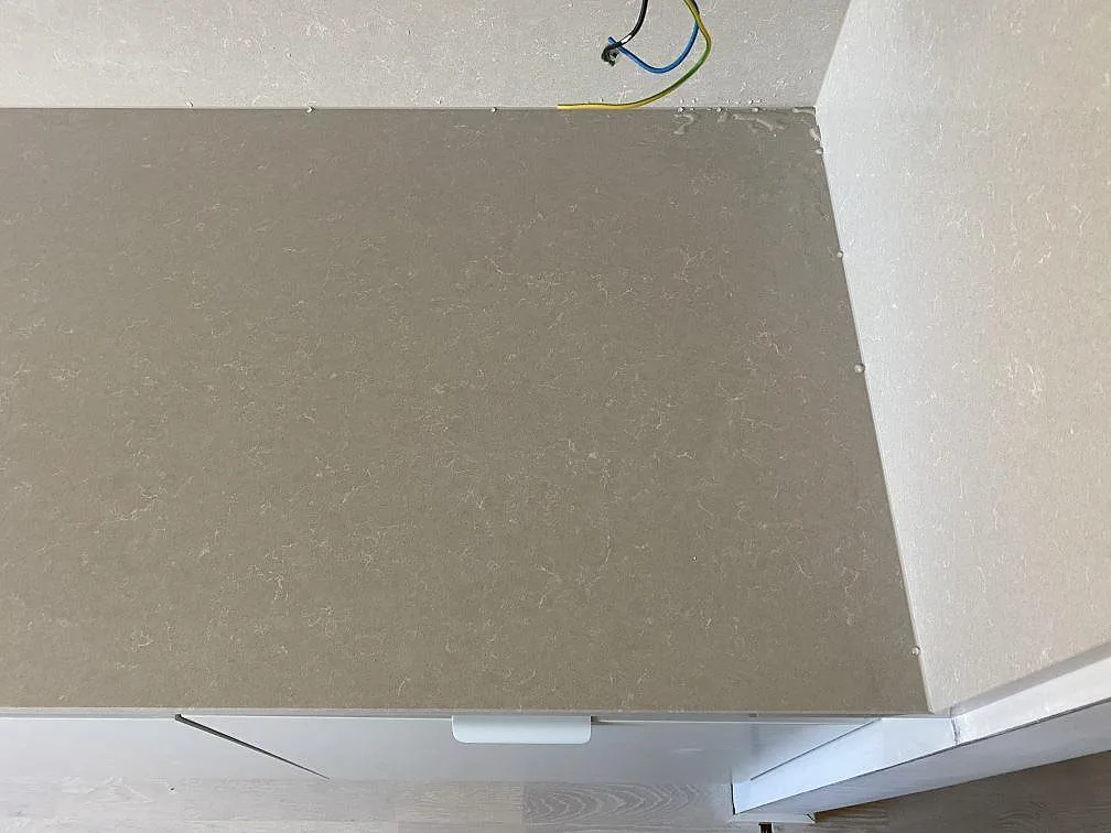Hörndetalj av polerad Technistone Noble Ivory White, komposit, där bänkskiva möter väggbeklädnad i köket i Lomma.