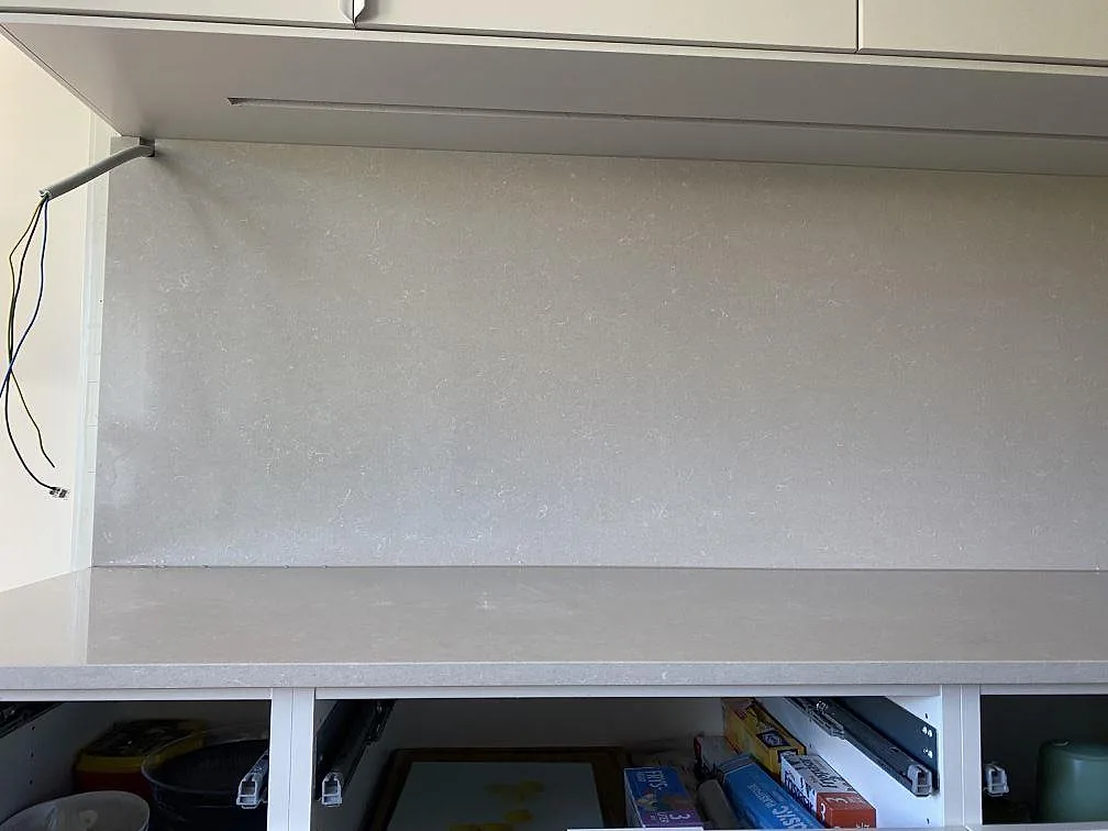Frontvy av köksbänkskiva i polerad Technistone Noble Ivory White, komposit, med väggbeklädnad och vita köksstommar i Lomma.