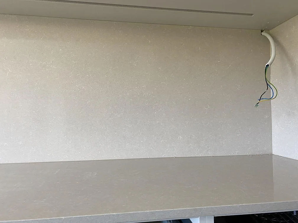 Detalj av polerad Technistone Noble Ivory White, komposit, som bänkskiva och väggpanel vid kabeluttag i ett kök i Lomma.