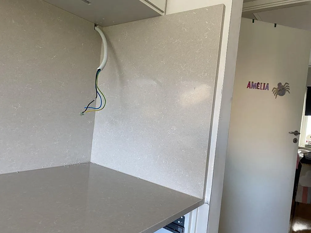 Sidovy av polerad Technistone Noble Ivory White, komposit, med bänkskiva och väggbeklädnad runt köksnisch i Lomma.