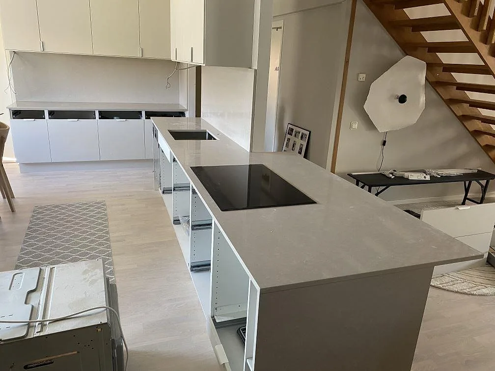 Köksbänkskiva och köksö i polerad Technistone Noble Ivory White, komposit, med häll och väggbeklädnad i ett kök i Lomma under montering.