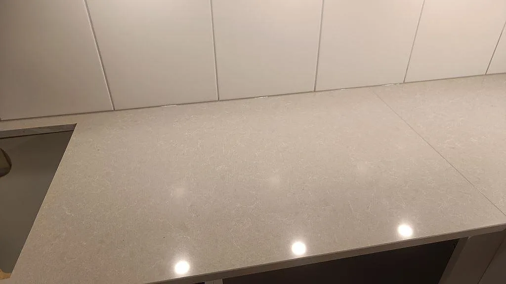 Detalj av polerad Technistone Noble Ivory White kompositbänkskiva med diskret ådring och vitt kakel i Lund.