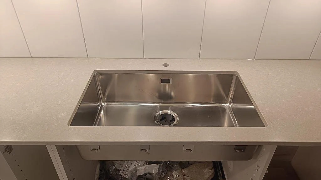 Närbild på underlimmad rostfri diskho i polerad Technistone Noble Ivory White kompositbänkskiva i Lund.