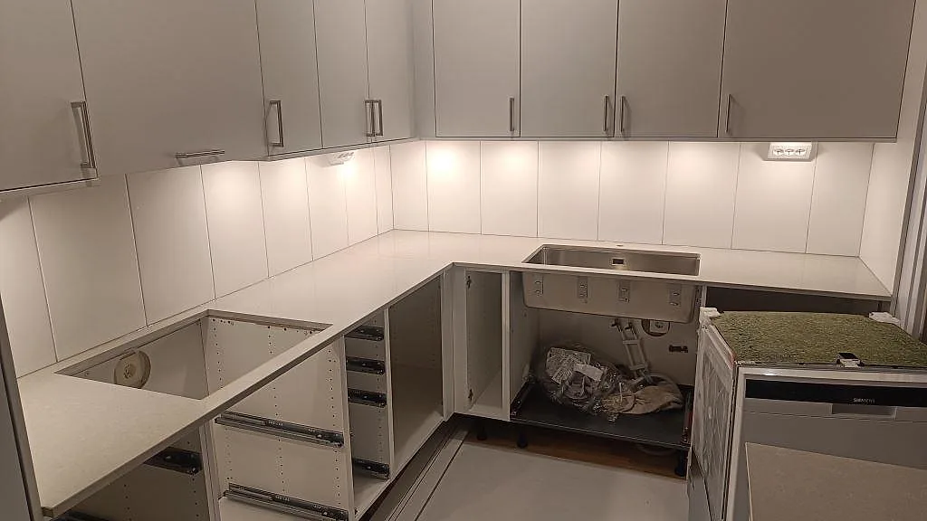 Köksbänkskiva i polerad Technistone Noble Ivory White med hälluttag och underlimmad rostfri diskho i ett vitt kök i Lund.