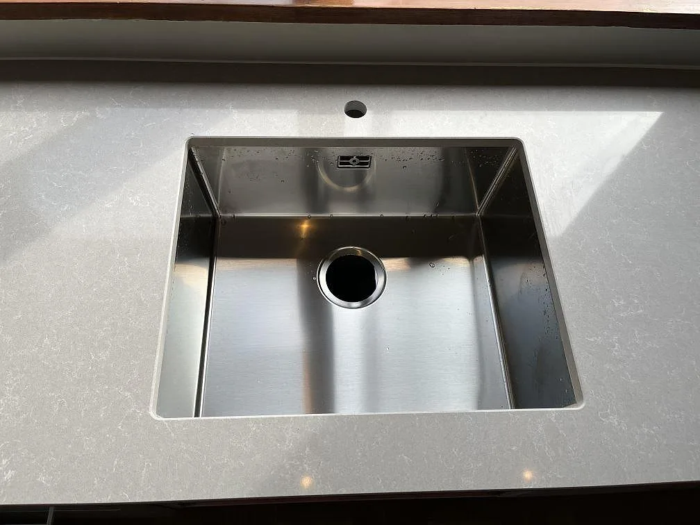 Underlimmad rostfri diskho i köksbänkskiva av Technistone Noble Ivory White, polerad ljusgrå kvartskomposit, i ett kök i Malmö.