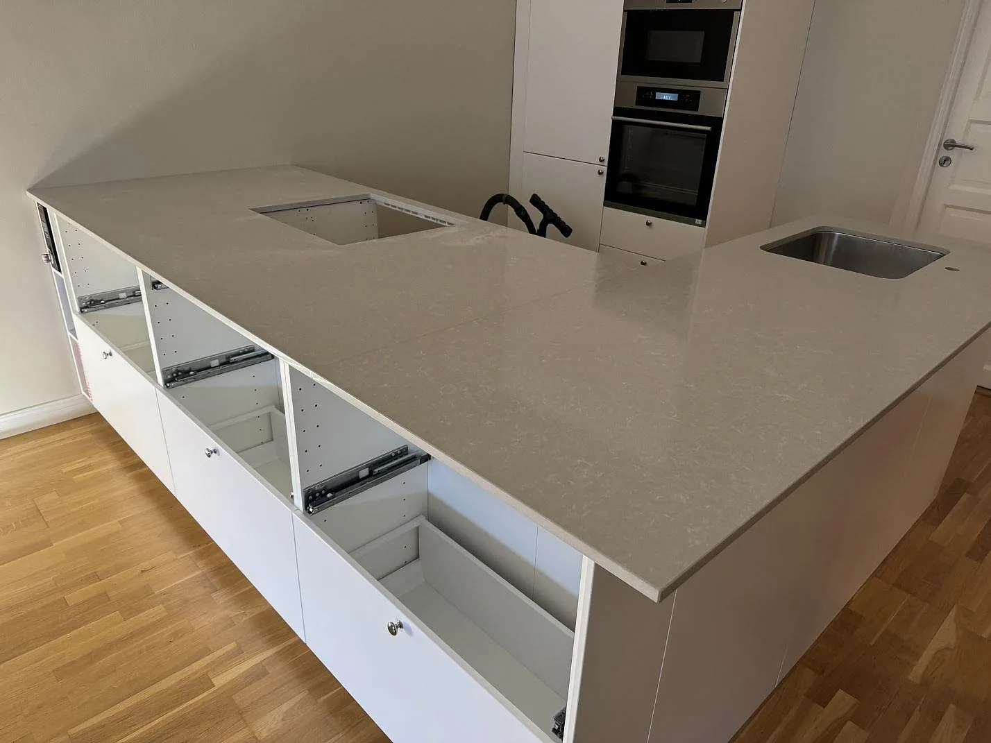 Bred köksö och bänkstråk i polerad Technistone Noble Ivory White med rektangulärt urtag, vit köksinredning och rostfri diskho i Malmö.