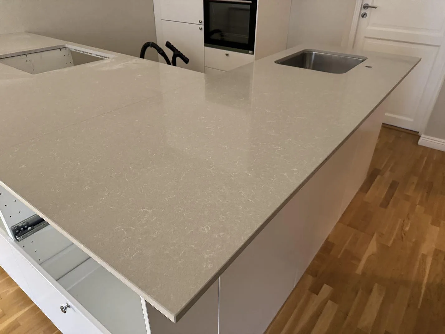 Närmare vy av köksö i polerad Technistone Noble Ivory White med ljus kvartskomposit, rostfri diskho och vit köksinredning i Malmö.