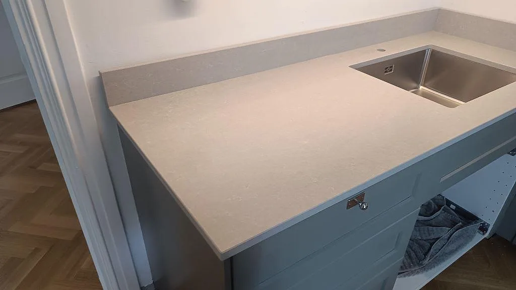 Peninsula med köksbänkskiva i polerad Technistone Noble Ivory White och rostfri diskho på grå stommar i Malmö.