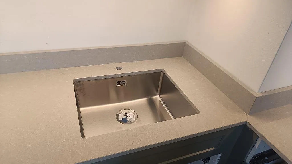 Närbild på underlimmad rostfri diskho i polerad Technistone Noble Ivory White med uppvikt stänkkant i Malmö.