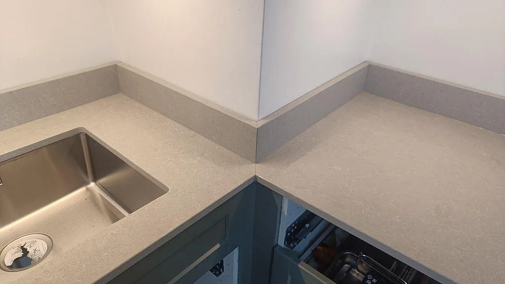 Hörnvy av köksbänkskiva i Technistone Noble Ivory White, polerad kvartskomposit, med stänkkant och diskho i Malmö.