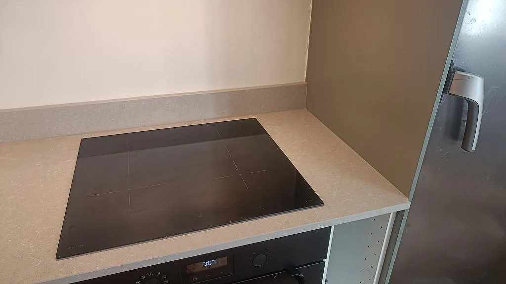 Svart häll i köksbänkskiva av polerad Technistone Noble Ivory White intill kyl i ett kök i Malmö.