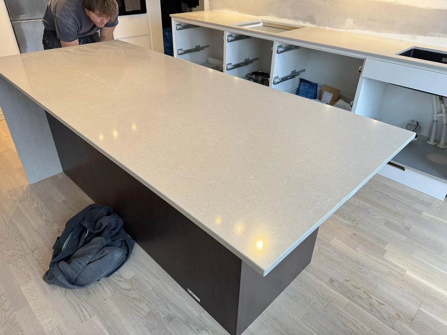 Bred köksö i polerad Technistone Noble Ivory White med ljus spräcklig yta och öppen köksinredning under montering i Malmö.